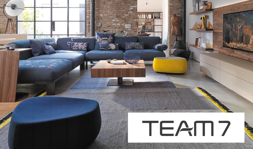 Team 7 Wohnzimmer mit blauem Sofa und Logo